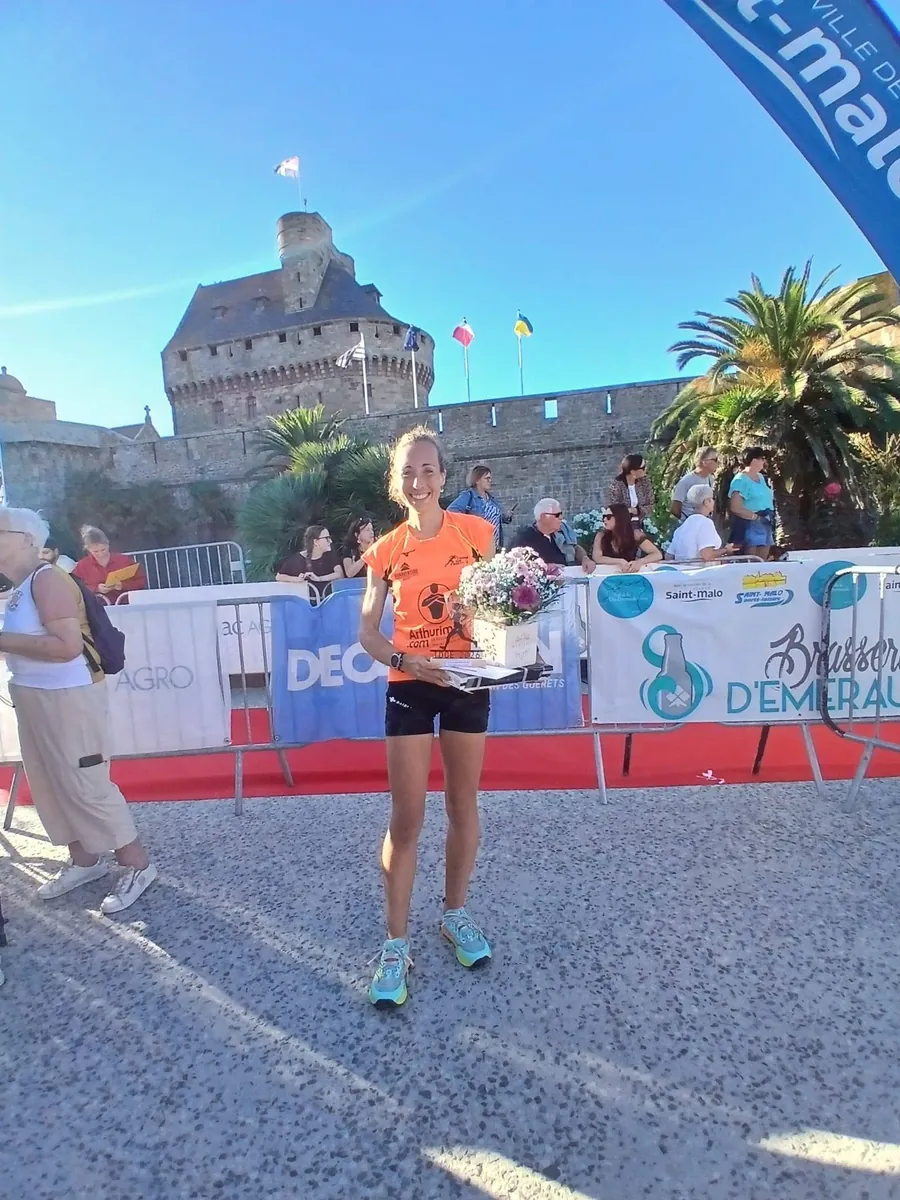 Une coureuse de Courir sur Brest sur le podium à Saint-Malo, bouquet et trophée en main