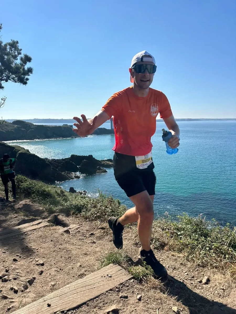 Un coureur de Courir sur Brest en maillot du club sur un sentier côtier, dossard au ventre
